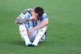 Lionel Messi duduk di lapangan rumput dengan kepala menunduk sambil memegang wajahnya.